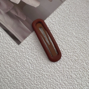 Close-up of matte dark brown fabric hair clip on a minimalist textured background