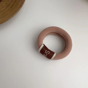 Detail of high-elasticity dusty pink hair tie featuring a brown Smile fabric label