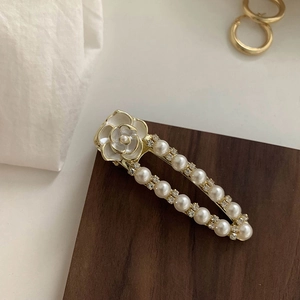 Detail of camellia hair clip with white pearls and gold metal on dark wood base