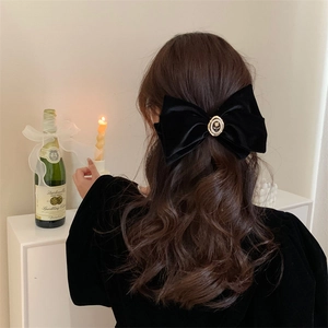 Detail of a large black velvet bow hair clip with a pearl rose metal centerpiece on hair