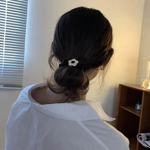 Minimalist black velvet hair tie with cream flower detail worn on a low hair bun