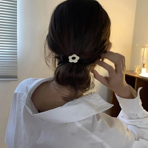 Elegant black velvet hair scrunchie with white flower accessory on a low bun hairstyle