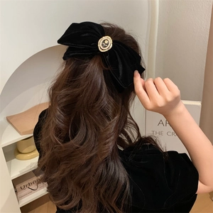 Detailed close-up of large black velvet bow hair clip with pearl rose center on hair