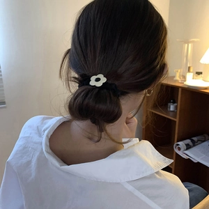 Black velvet hair scrunchie with white flower detail shown on model in home setting