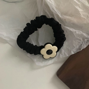 Detail of a black velvet scrunchie with a cream flower accessory on white paper