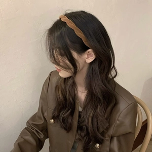 Serre-tête tressé en velours marron porté par un mannequin aux longs cheveux bouclés