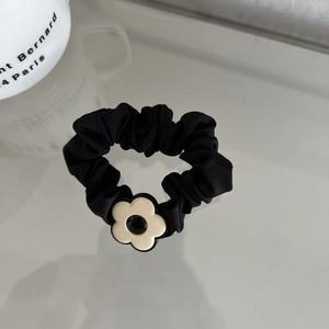 Close-up of black satin scrunchie with a cream flower pendant on a clean white surface