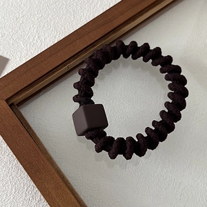 Detailed macro view of deep brown spiral elastic hair tie with matte square bead decorative