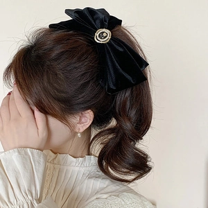 Close-up of black velvet oversized bow hair clip with gold rose and pearl button detail