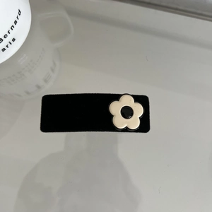 Detail of a black velvet rectangular hair clip with a classic white and black resin flower