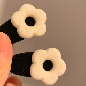 Detailed view of two velvet flower hair clips featuring white plush petals on black clips