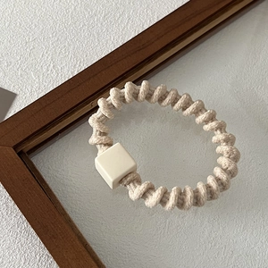 Detailed close-up of oatmeal fabric spiral hair tie with a matte square charm