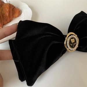 Detailed close-up of a velvet bow hair clip with pearl-inlaid gold rose centerpiece