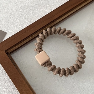 Detailed view of brown spiral hair tie with square resin bead on a textured surface