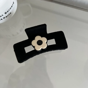 Detail of a black flocked hair claw clip featuring a minimalist cream flower design