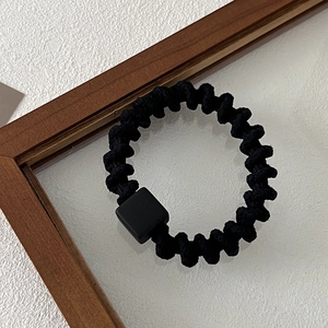 Detail shot of black spiral elastic hair tie with a matte square block in a minimalist setting