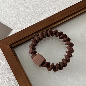 Detailed view of dark brown spiral hair tie with a matte square charm on wooden background