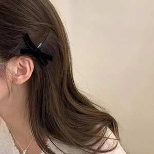 Close-up of a minimalist black velvet bow hair clip worn on the side of brown wavy hair