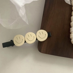 Detail of a black hair clip featuring three matte cream yellow smiley face patterns