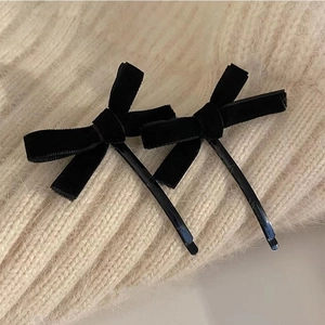 Detail shot of a pair of black velvet bow hair clips on a soft beige knitted fabric