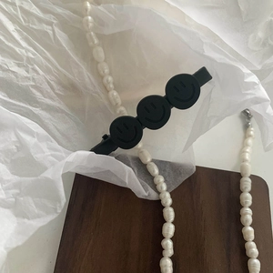 Detail of matte black smiley face hair clip with a strand of elegant freshwater pearls