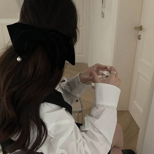 Détail d'une grande pince à cheveux en velours noir ornée d'une perle blanche pendante