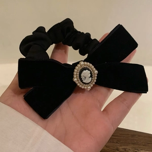 Close-up of black velvet bow scrunchie with vintage cameo and pearl accent