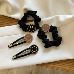 Détail d'un ensemble de quatre chouchous et barrettes noirs avec motifs smiley dorés