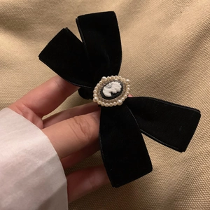 Close-up of black velvet bow hair tie with vintage cameo pendant and pearl detailing