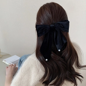 Rear view of a large black velvet bow hair clip with pearl accents on long wavy hair