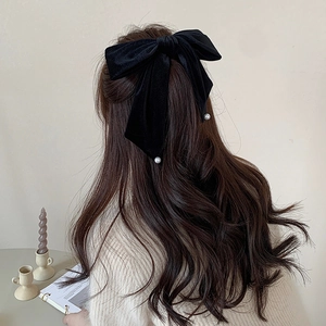 Large vintage black velvet bow hair clip with elegant pearl accents on curly hair