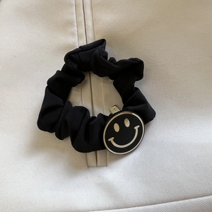 Gros plan d'un chouchou noir élastique avec un pendentif smiley au bord doré