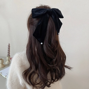 Close-up of a large black velvet bow hair clip with white pearls on wavy brown hair
