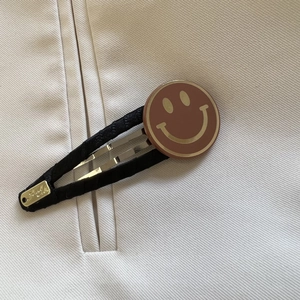 Détail de la pince à cheveux noire en tissu avec smiley doré et étiquette fait main