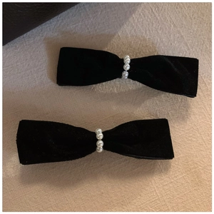 Detail of two black velvet bow hair clips with white pearl center on a linen background