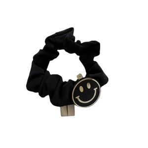 Chouchou en tricot noir avec un pendentif sourire en métal doré sur fond blanc