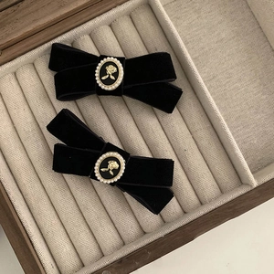Pair of black velvet bow hair clips with vintage embossed pearl roses on wood background