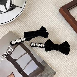 Elegant pair of black velvet bow hair clips with rhinestones on white fabric