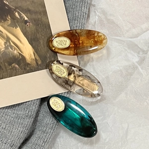 Detail of three marble texture acetate hair clips in amber, grey, and green colors