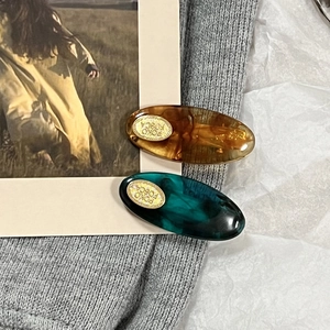 Macro detail of tortoiseshell and teal marble hair clips with golden oval logo plate