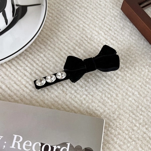 Detailed close-up of a black velvet bow hair clip with three sparkling rhinestones on fabric