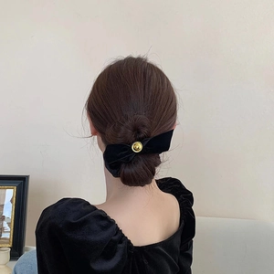 Detail view of a black velvet bow hair clip with a gold button on a model hairstyle