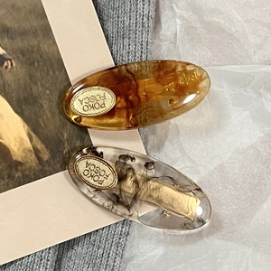 Macro shot of oval acetate hair clips with marble texture and golden metal logo plate