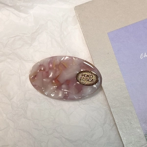 Détail d'une pince à cheveux ovale en acétate rose marbré avec un logo en métal doré