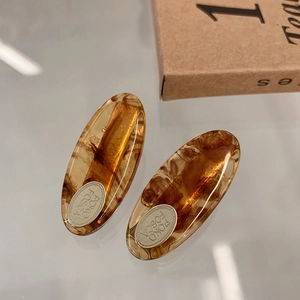 Detailed macro view of amber acetate oval hair clips with silver metal logo plaque