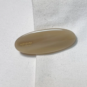 Vue détaillée d'une pince à cheveux ovale en acétate beige avec logo France Handmade doré