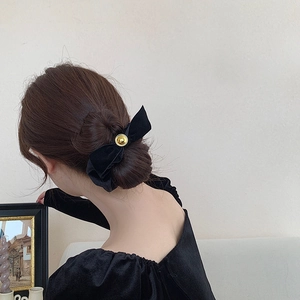 Detail of a black velvet bow hair clip with gold metal buckle on a bun hairstyle
