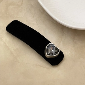 Detail of a vintage black velvet hair clip with a grey heart-shaped crystal on white texture