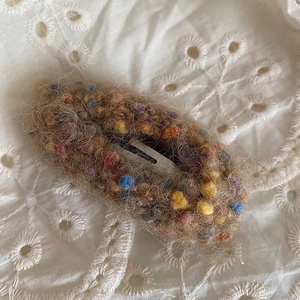 Macro d'une pince à cheveux en peluche marron avec boules de laine sur tissu brodé