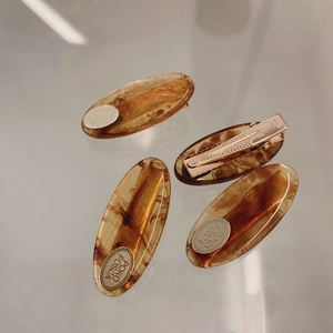 Close-up of four amber acetate oval hair clips with engraved gold metal accents